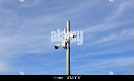 A pair of closed-circuit television bullet cameras are installed at different angles on a galvanized steel post with communication equipment against Stock Photo