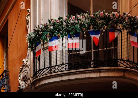 An elegant residential balcony decorated with rows of the French tricolor flag and a lush garland of roses. Stock Photo