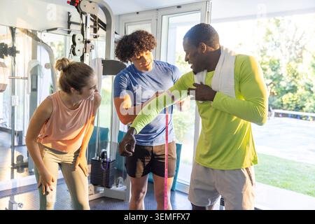 Diverse fitness group measuring upper arm using pink tape at gym cable machine in sportswear Stock Photo