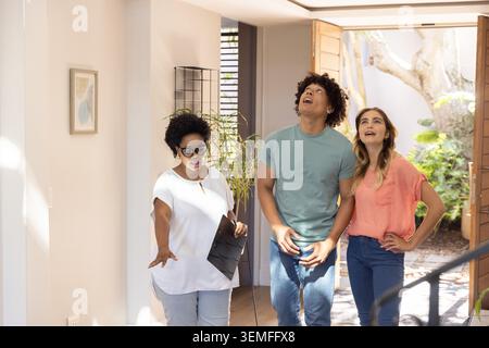 Diverse group touring foyer with host in white top gesturing, holding black folder, open front door Stock Photo