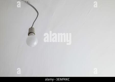 Single light bulb hanging from a wire on a white ceiling Stock Photo