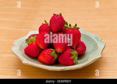 Fresh ripe strawberries arranged on a light ceramic plate on a wooden table in Japan. Stock Photo