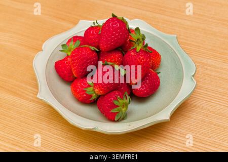Fresh red strawberries with green leaves served on a small ceramic plate on a wooden surface in Japan. Stock Photo