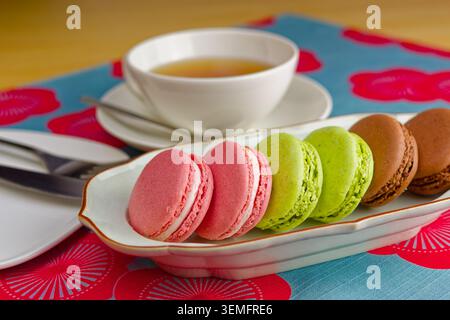 Colorful French macarons served on a plate with a cup of tea on a bright patterned table in Japan. Stock Photo