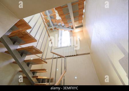 low-angle shot captures modern stairs with wooden steps and metal supports, against a textured beige wall with a tall window. Stock Photo
