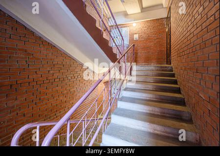 stairwell with brick walls and a pink metal railing. Concrete stairs lead upwards Stock Photo