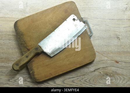 old rusty cleaver chop knife on wooden cutting board at table Stock Photo