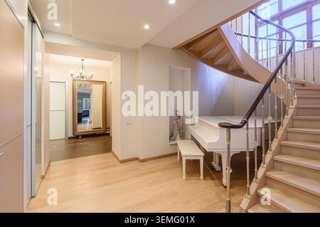 Elegant hallway with a piano, staircase, and large mirror, featuring light wood floors and a sophisticated design. Stock Photo