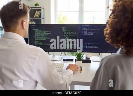 Developers collaborating on code at dual monitors in office, programming team Stock Photo