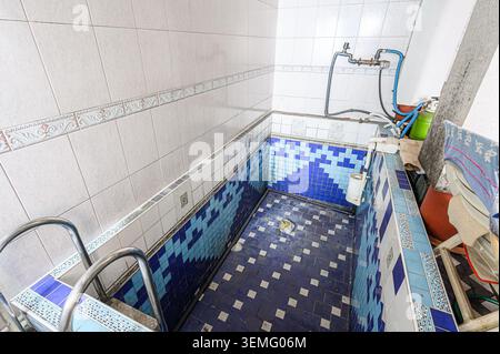 indoor tile-lined pool/tub area with blue and white patterns, plumbing fixtures, and some clutter. It appears somewhat aged and perhaps unused recentl Stock Photo