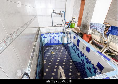 indoor tile-lined pool/tub area with blue and white patterns, plumbing fixtures, and some clutter. It appears somewhat aged and perhaps unused recentl Stock Photo