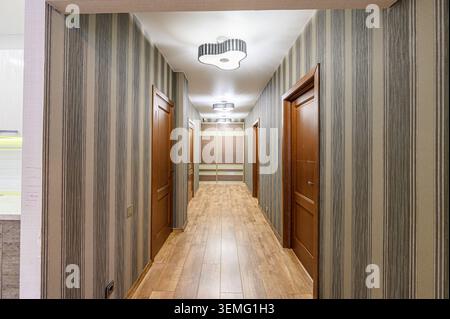 hallway with striped wallpaper, wooden doors, wood-like tile flooring, and decorative lighting fixtures Stock Photo