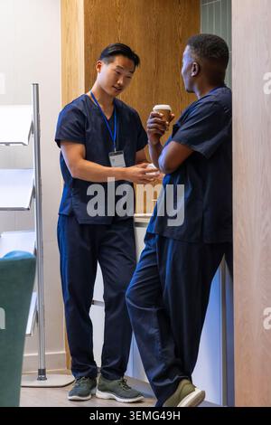 Diverse male staff wearing navy scrubs chatting in break area, holding coffee and ID badge Stock Photo