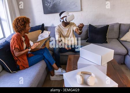 African American couple sitting on gray sectional sofa interacting with VR headset and tablet boxes Stock Photo