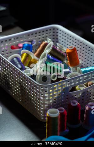 Sewing thread assortment in a white plastic basket in a dark setting Stock Photo