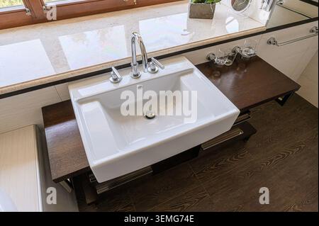 bright bathroom sink with a chrome faucet and brown countertop. Natural light from the window reflects on the marble sill. Stock Photo