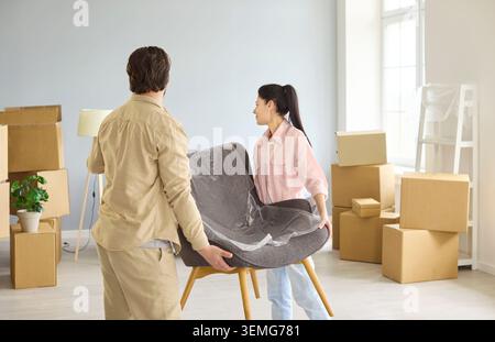 Smiling couple lifting chair among boxes on moving day in new home apartment Stock Photo
