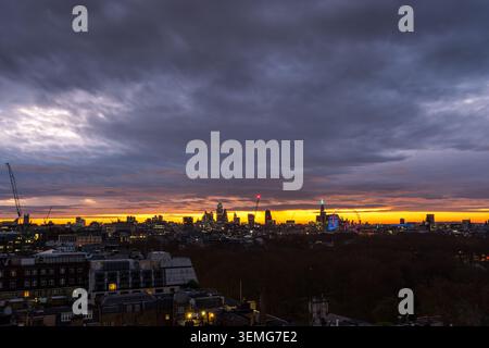 Moody dawn over London with heavy dark clouds and a glowing golden strip of light along the horizon behind the city skyline, England, UK Stock Photo