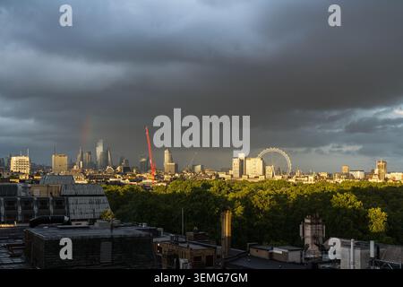 Stormy sky with a rainbow over the London skyline, the City of London skyscrapers and the London Eye beneath dark rain clouds, England, UK Stock Photo