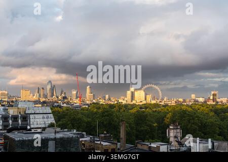 London skyline beneath a dramatic cloudy sky with the City of London skyscrapers, the London Eye and green parkland in the foreground, England, UK Stock Photo