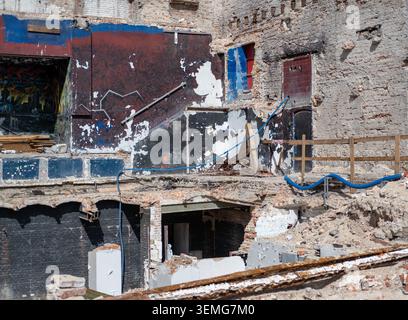 Demolished urban structure reveals interior walls, rubble, and concrete foundations in sunlight. Stock Photo
