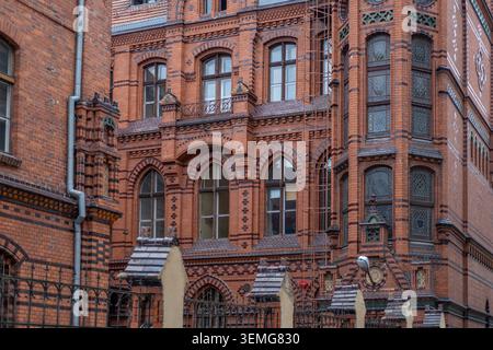 Detailed facade of a historic red brick building is displaying arched windows, a rusty iron fire escape ladder, and decorative masonry. Stock Photo