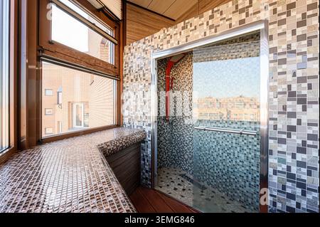 Modern bathroom featuring mosaic tiles, a glass shower stall, and a large window with a tiled sill. Stock Photo