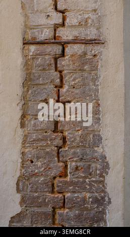 Exposed red brick wall section is visible through cracked plaster interior finish at a historic building restoration site. Stock Photo