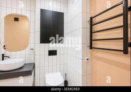 modern bathroom features white vertical tiles with dark grout, contrasting with black storage and fixtures. A beige wall adds warmth. Stock Photo