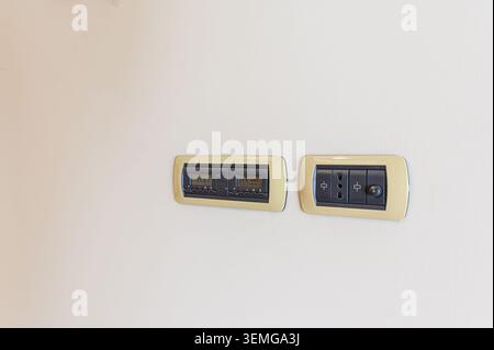 Two electrical panels are installed on a white wall. One contains a digital control panel, and the other has electrical outlets with a switch. Stock Photo