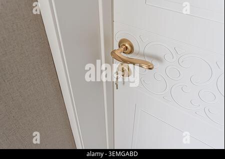 Close-up of a white door with decorative swirls, a gold handle, and keys inserted Stock Photo