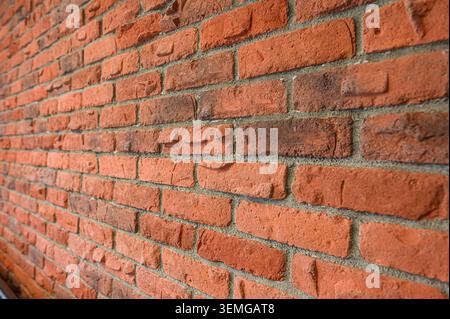 brick wall is shown at an angle. The bricks are predominantly reddish-orange with some darker, mottled sections Stock Photo