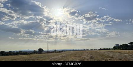 Sun rays breaking through clouds above the countryside near Rome, Italy, creating a dramatic rural landscape. Stock Photo
