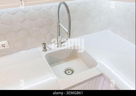 bright kitchen sink with a stainless steel faucet and a soap dispenser. Backsplash features hexagonal tiles. Stock Photo