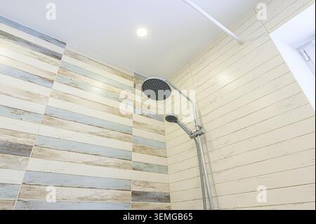shower area with wood-look tiles in light colors, a chrome shower head and hand shower, and a bright recessed light. Stock Photo