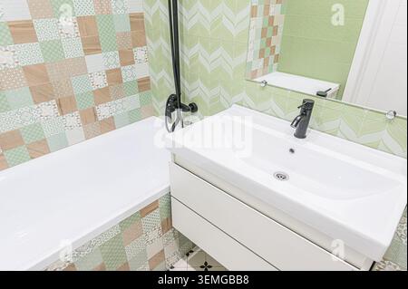 modern bathroom featuring a white sink vanity, a white bathtub, and green and brown patterned tiles Stock Photo
