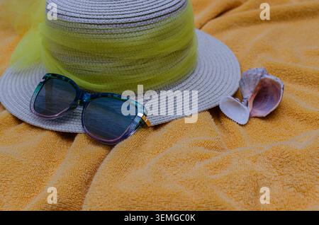 A flat lay composition of summer holiday essentials featuring a stylish straw hat with a yellow ribbon, trendy sunglasses, and a natural seashell rest Stock Photo