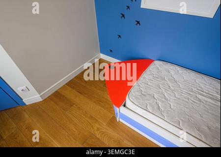 corner of a room features a bed with a white mattress and an orange headboard against a blue wall decorated with bird silhouettes. Wooden flooring and Stock Photo