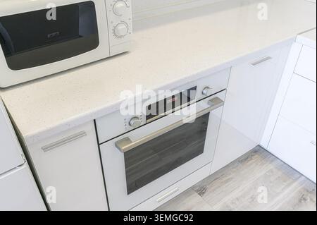 pristine white kitchen corner featuring a microwave and built-in oven set against a speckled countertop and sleek white cabinets. Stock Photo