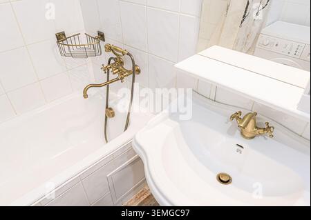 Bright bathroom scene with white tiles, a white sink, a tub, and vintage-style bronze faucets. Stock Photo