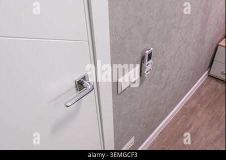 Close-up of a modern interior featuring a white door with a chrome handle, textured grey wall, switches, and a remote control mounted on the wall. Stock Photo
