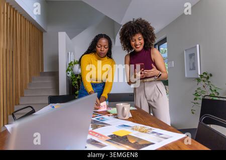 African American female coworkers collaborating on layout at studio, arranging swatches, laptop. Teamwork, design, moodboard, modern, workspace, woode Stock Photo