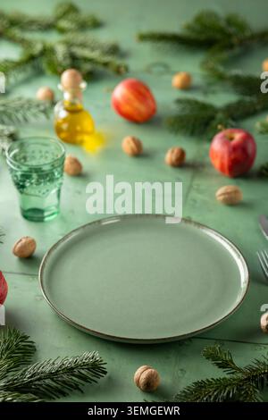 Festive table setting with an empty plate, pine branches, apples, and walnuts, creating a holiday atmosphere Stock Photo