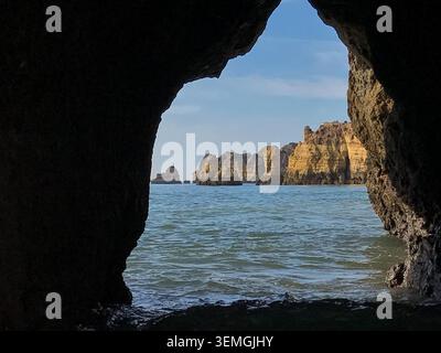 View from inside a natural sea cave looking out toward the stunning coastline. Blue Atlantic waters meet the famous golden sandstone cliffs and rocks. Stock Photo