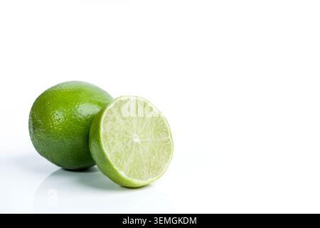 A vibrant green lime is shown whole next to its juicy, sliced half, isolated on a clean white surface Stock Photo
