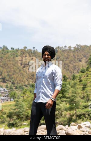 A vertical three quarter portrait of a smiling young Sikh man in formal clothes looking at the camera while posing in scenic Himachal Pradesh. Stock Photo