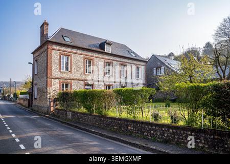 A large two story historic building features a stone and red brick facade with a dark slate roof. A lush green garden with hedges and a metal fence bo Stock Photo