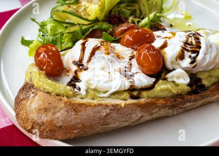 Poached eggs and roasted cherry tomatoes on avocado sourdough toast, drizzled with balsamic glaze Stock Photo