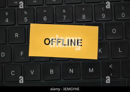 A yellow note with the word OFFLINE typed on it placed on a black laptop keyboard. Close up. Stock Photo