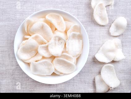 Prawn crackers, shrimp chips in a white bowl on linen. Deep-fried crackers made from a dough of tapioka, ground prawns, and seasonings. Stock Photo
